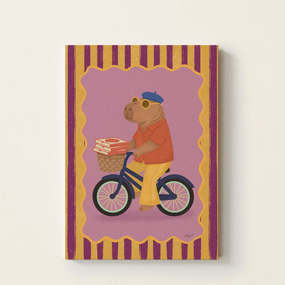 Capybara on bicycle poster featuring a capybara wearing sunglasses and a beret riding a bicycle with pizza boxes in a basket on a colorful background.