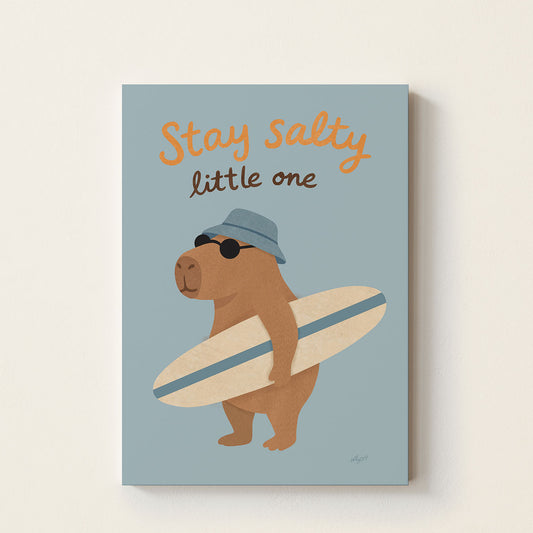 Hand-drawn capybara wearing sunglasses and a blue bucket hat while holding a surfboard beneath the words "Stay Salty Little One", whimsical coastal wall art for nurseries, bedrooms, and playrooms.